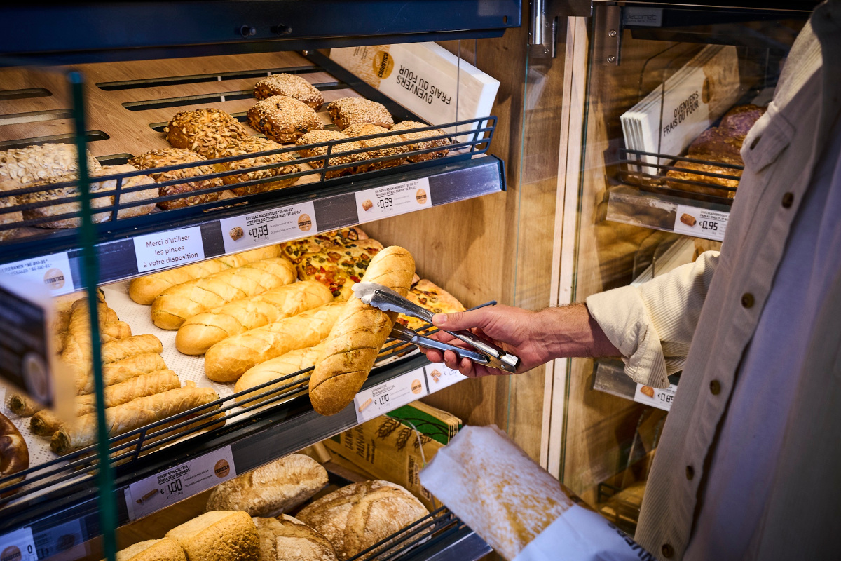 Mano con pinza preleva pane fresco dal banco espositore di un retail: vendite di pane in Italia per 3,8 miliardi di euro