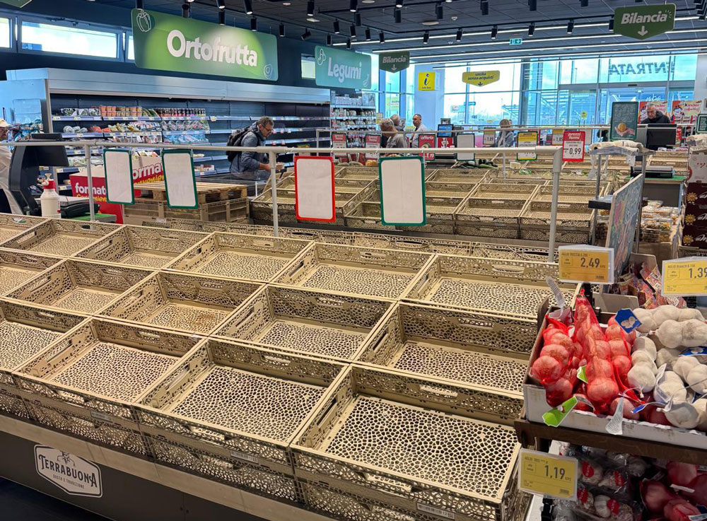 Scaffali vuoti nel reparto ortofrutta del supermercato: cassette di legno senza merce per il blocco dei trasporti.