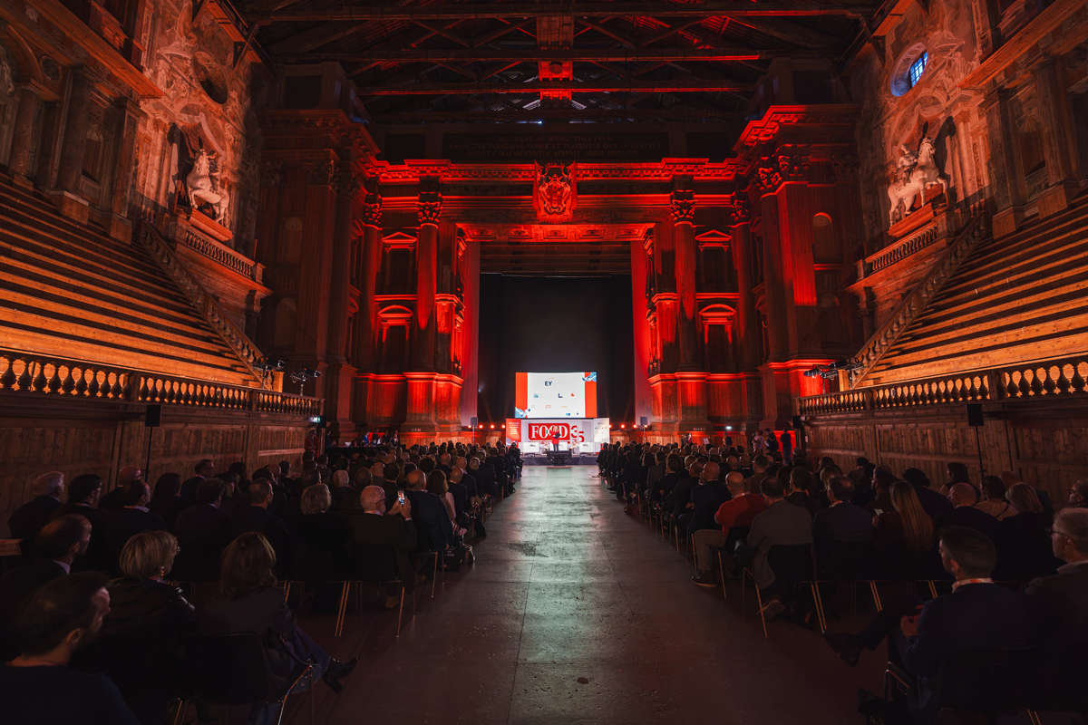 Grande auditorium storico con pubblico seduto e palco illuminato di rosso durante un evento TEDx.