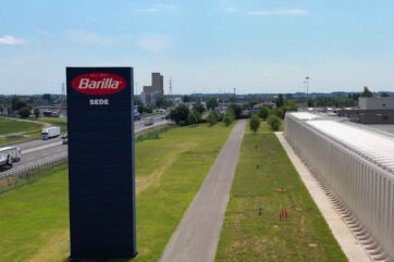 Barilla plant in Pedrignano, Parma: tall Barilla Sede sign, warehouse and highway, supporting automated truck loading intralogistics.