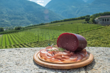 Bresaola della Valtellina PGI on wooden board with mountain vineyard backdrop. Cured beef, Italian food.