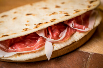 Piadina Romagnola PGI with prosciutto. Italian flatbread sandwich filled with cured ham. Delicious street food.