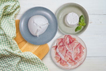 Italian food: burrata, ricotta, prosciutto on plates with a cutting board and a checkered cloth. San Daniele