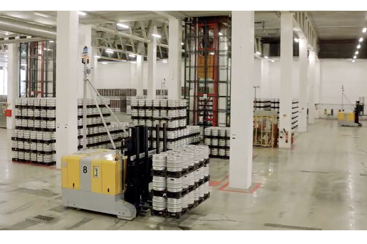 Warehouse interior with forklift carrying kegs. Block storage area with stacked barrels.