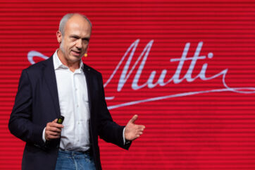 CEO Francesco Mutti presenting Mutti tomato products. Red background with Mutti logo. Business presentation.