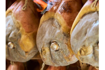 Hanging Prosciutto di Parma hams. Italian dry-cured pork with DOP fire branding. Delicious charcuterie meat.