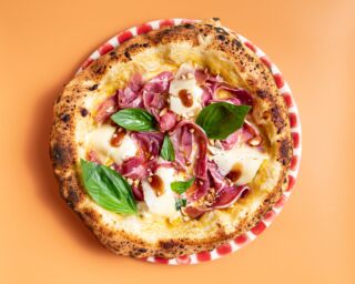 Giuseppe Cutraro's pizza, from Paris. Gourmet pizza with basil, prosciutto, cheese, and balsamic glaze on a red and white plate.