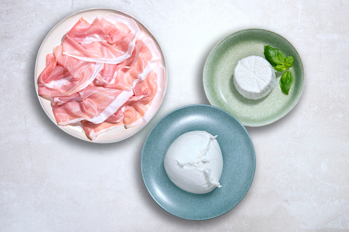 Overhead shot of Mozzarella di Bufala Campana PDO, Prosciutto di San Daniele PDO, Ricotta di Bufala PDO on plates.