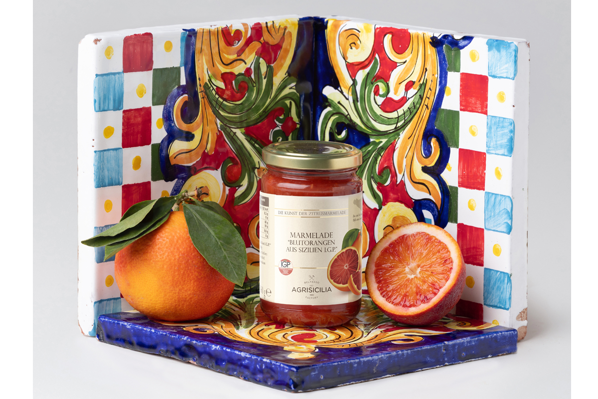 Agrisicilia blood orange jam jar with fresh oranges on a colorful Sicilian tile. Gourmet food product.