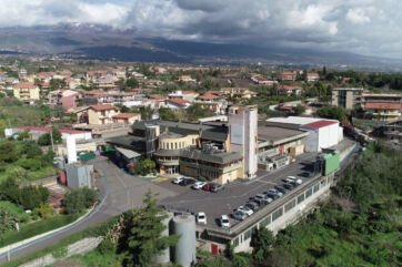 Beltè Italian Iced Tea factory acquired by Sibat Tomarchio. Facility with parking and Mount Etna in background.