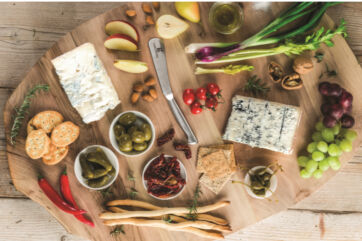 Gorgonzola cheese board with crackers, fruit, nuts, olives, peppers, tomatoes, and breadsticks. Appetizer platter.