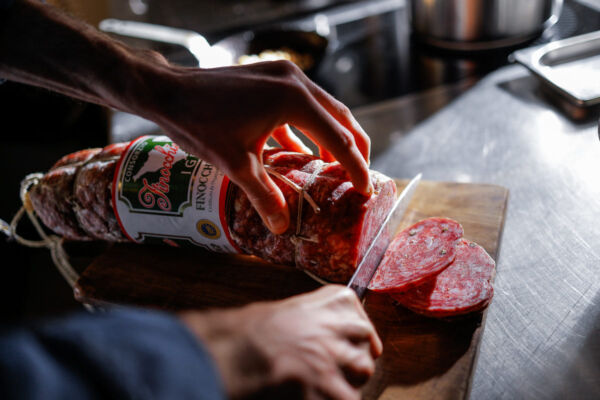 Slicing Finocchiona PGI. Close-up of Italian salami being sliced on a wooden board. Delicious cured meat.