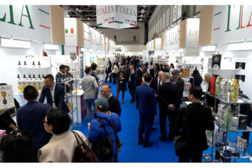 Foodex Japan: Italian food expo with crowds of people at booths. Italian food and drink products on display.