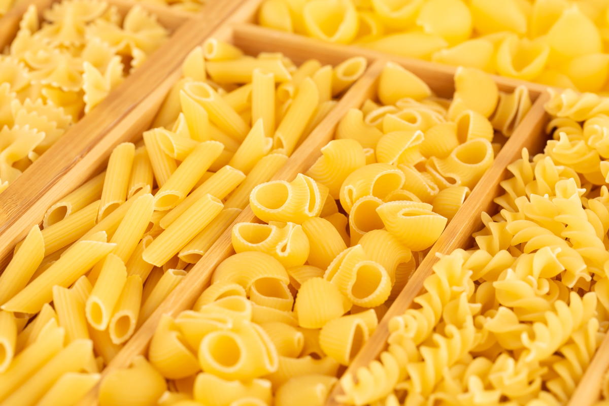 Italian food exports-Unionfood-Unione Italiana Food-Assorted dry pasta. Penne, farfalle, shells, and fusilli pasta varieties in a wooden tray. Italian food background.