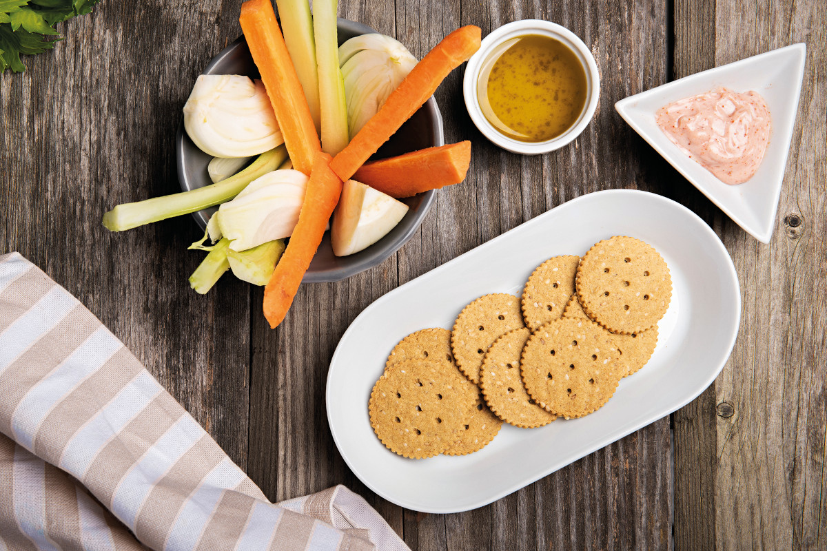 Crackers, carrots, celery, and dips on a rustic wooden surface. Healthy snack food.-Farmo