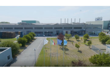 Exterior of Stabilimento di Pomposa, a large industrial building with flags. Manufacturing plant. - E80-Conserve Italia