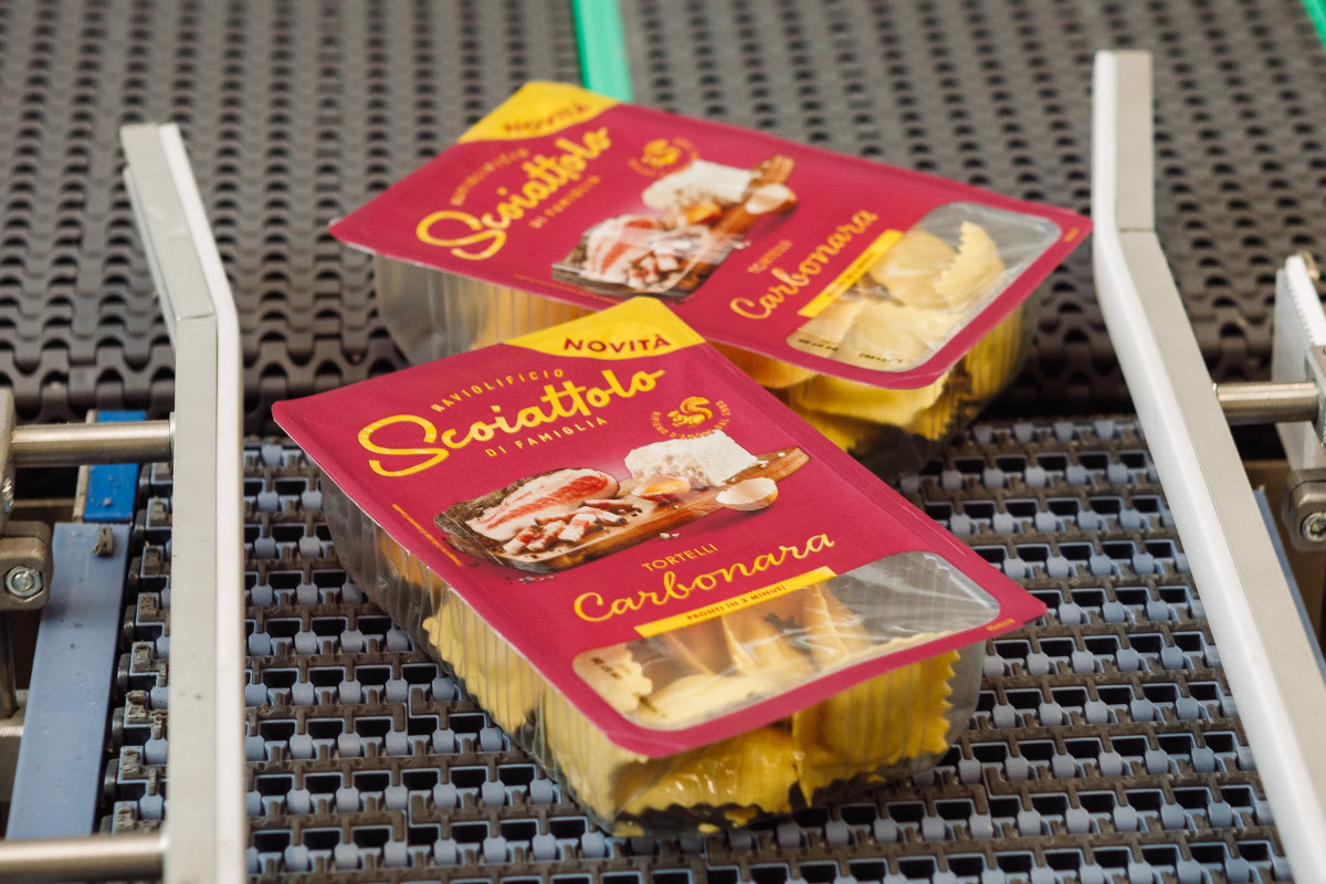 Packaged Tortelli Carbonara pasta on a conveyor belt. Raviolificio Scoiattolo brand. Fresh pasta product.