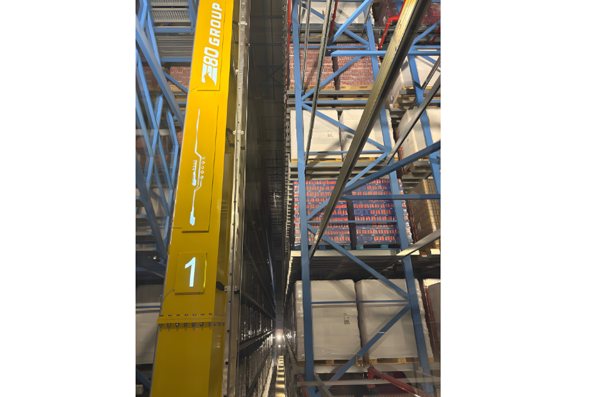 Yellow automated storage and retrieval system crane operating in a high-density warehouse with blue industrial racking. - E80-Refresco