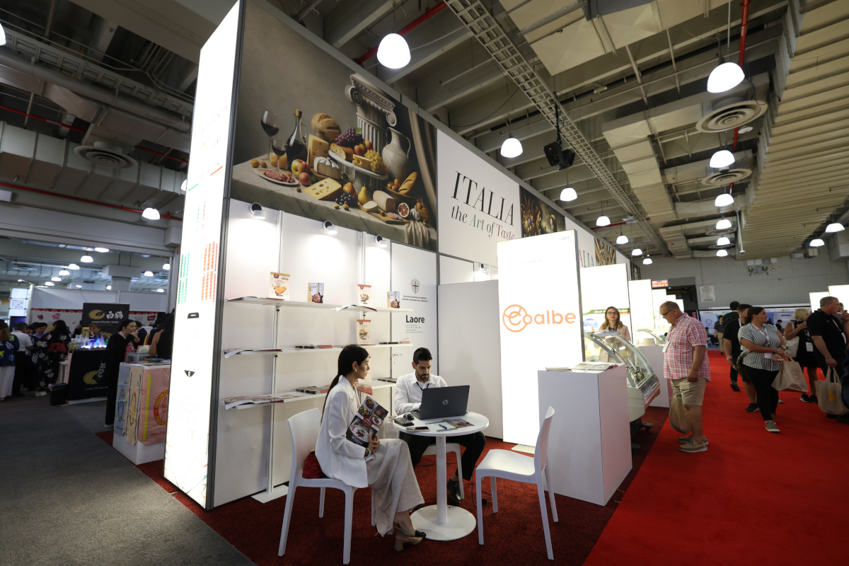 Exhibitors at the Italia the Art of Taste booth at a trade show, featuring Coalbe branding and Italian food photography.
