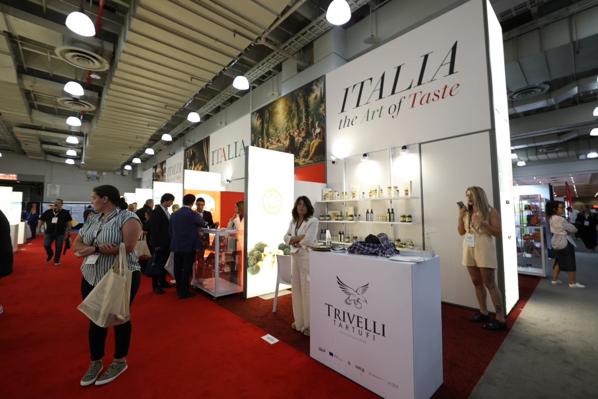 Exhibitors and attendees at the Italia the Art of Taste booth featuring Trivelli Tartufi at a professional food trade show.