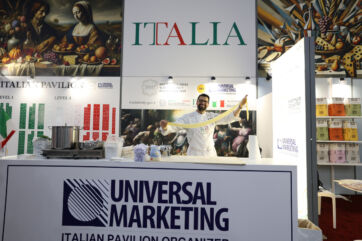 Chef in white uniform stretching fresh handmade pasta at the Universal Marketing Italian Pavilion booth at a food show.