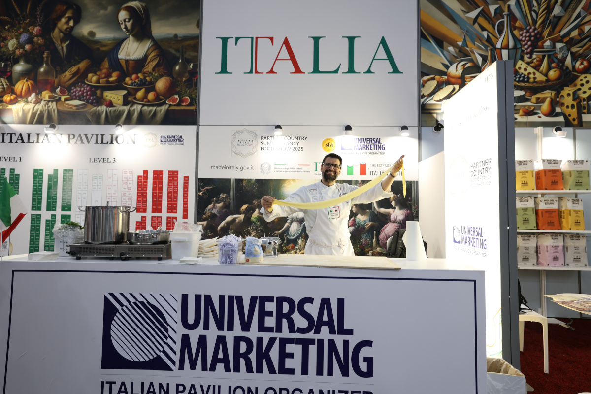 Chef in white uniform stretching fresh handmade pasta at the Universal Marketing Italian Pavilion booth at a food show.