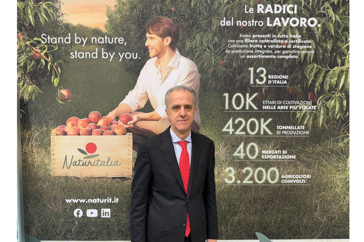 Augusto Renella standing in front of a Naturitalia promotional banner featuring peach orchard imagery and company statistics.