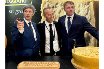 Three men in suits at the Summer Fancy Food Show promoting Parmigiano Reggiano PDO cheese at a branded booth.