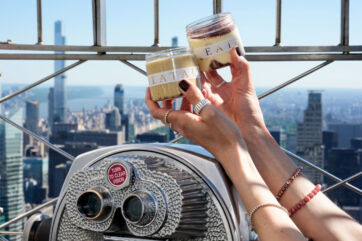 Hands holding Eataly dessert jars against the New York City skyline from the Empire State Building observation deck.