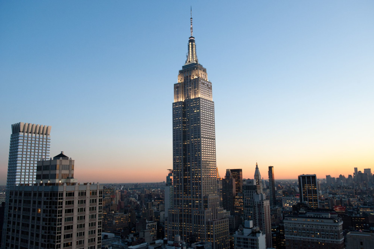 Empire State Building illuminated at sunset, towering over the New York City skyline with surrounding skyscrapers at dusk.