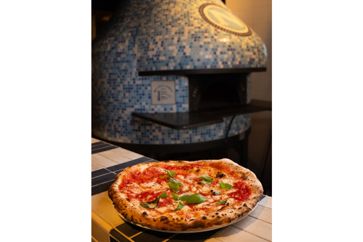 Freshly baked Margherita pizza with basil in front of a blue mosaic wood-fired oven at L'Antica Pizzeria da Michele.