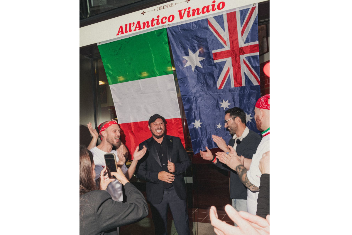 People cheering for a man in a suit in front of Italian and Australian flags at All'Antico Vinaio restaurant in Australia.