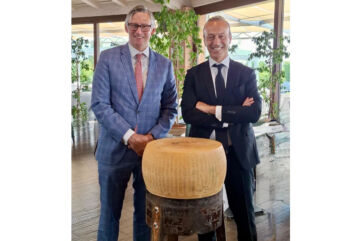 US Consul General Douglass Benning visits the Parmigiano Reggiano supply chain, standing with a wheel of Italian cheese.