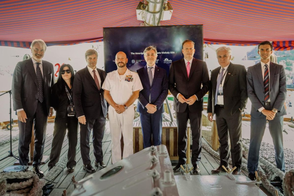 Group of officials and a naval officer posing for a photo at the Vinitaly USA event aboard the Amerigo Vespucci ship.