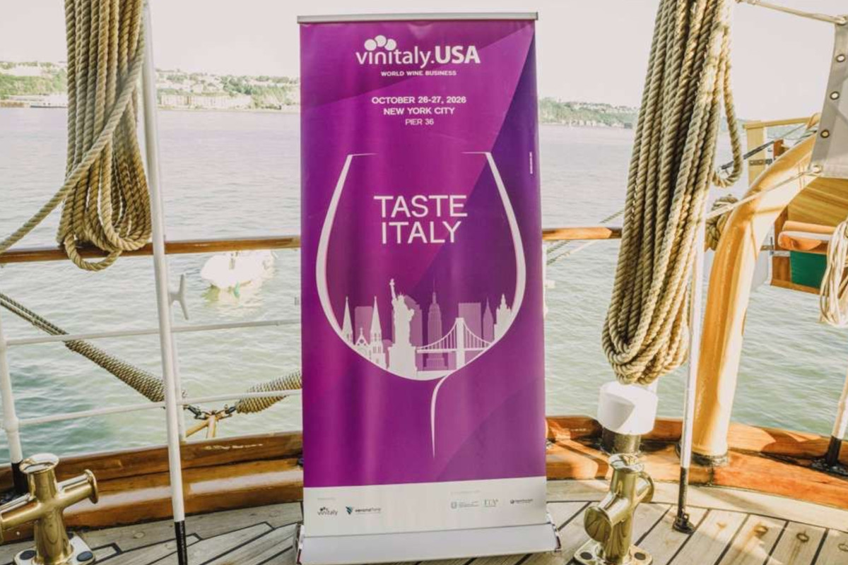 Vinitaly USA purple banner with Taste Italy branding and NYC skyline silhouette on a ship deck overlooking the water.