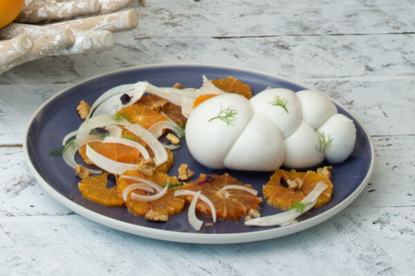 Fresh Mozzarella di Gioia del Colle PDO treccina served with sliced oranges, fennel, and walnuts on a blue plate.