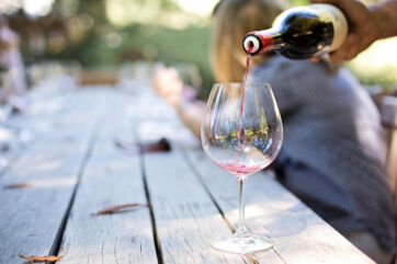 Red wine being poured from a bottle into a glass on a rustic wooden table at an outdoor Italian vineyard event. - Italian wine exports-Italian wine sector