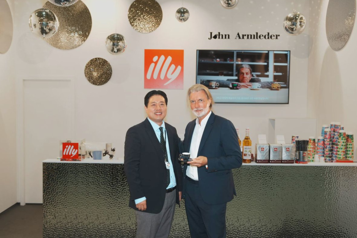 John Armleder and a colleague at the illy Art Collection booth during Frieze Seoul, featuring illy branding and decor.