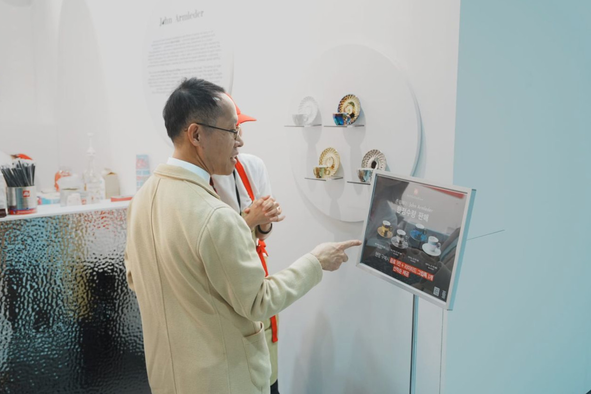 Man pointing at an illy Art Collection display by John Armleder featuring designer espresso cups at Frieze Seoul.