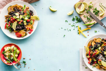 Whole Foods 2027 food trend flat lay: black beans, avocado, lime & veggies on blue tabletop.