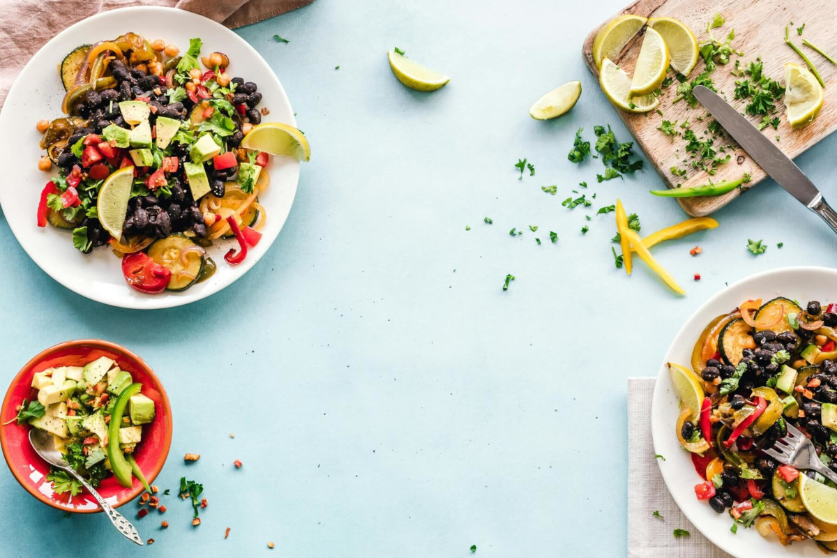 Whole Foods 2027 food trend flat lay: black beans, avocado, lime & veggies on blue tabletop.