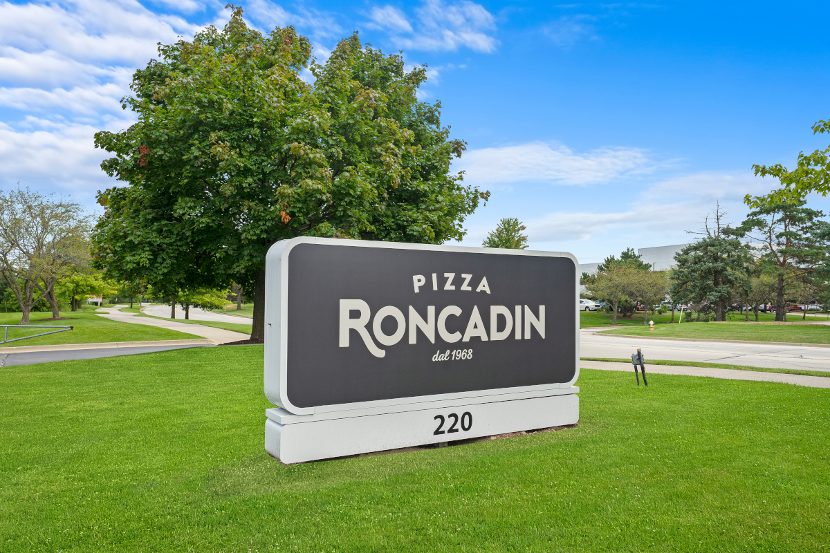 Pizza Roncadin sign on green lawn with trees and blue sky at Chicago location.
