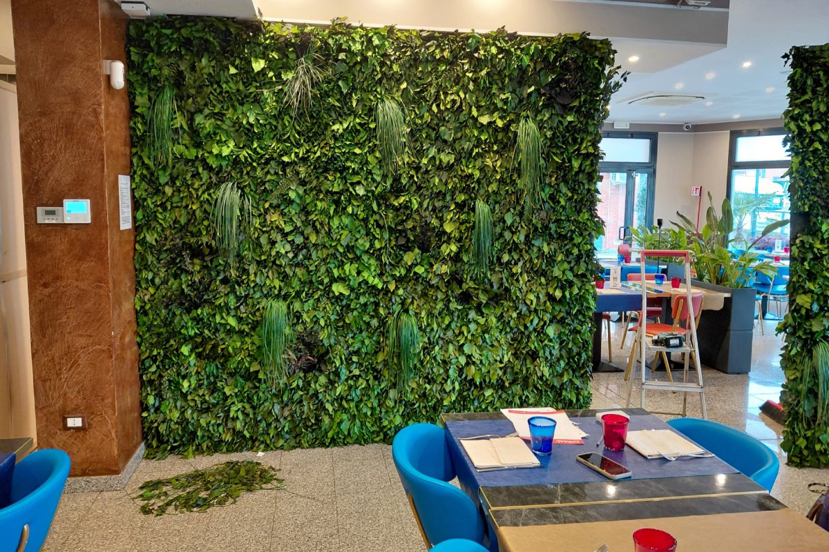 Parete di verde stabilizzato su misura per il design di un ristorante, con piante rigogliose e arredi moderni.