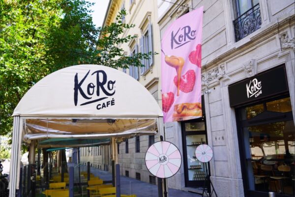 KoRo Café in Italia. Facciata del negozio KoRo con insegna, bandiera rosa e tavolini esterni.