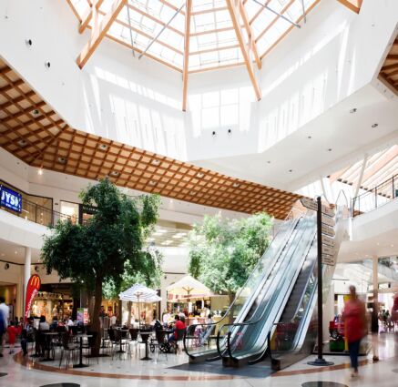 Area ristorazione in centro commerciale. Tavoli, sedie, scale mobili e lucernario.