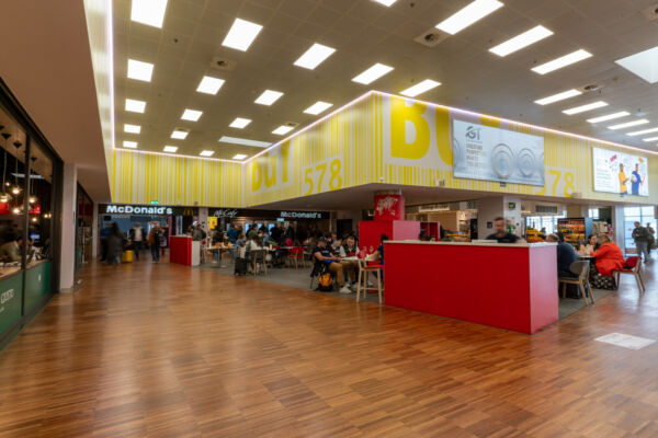 Food court affollata: McDonald's e ristoranti. Pavimento in legno, illuminazione moderna. Top 30 Food Service Power List.