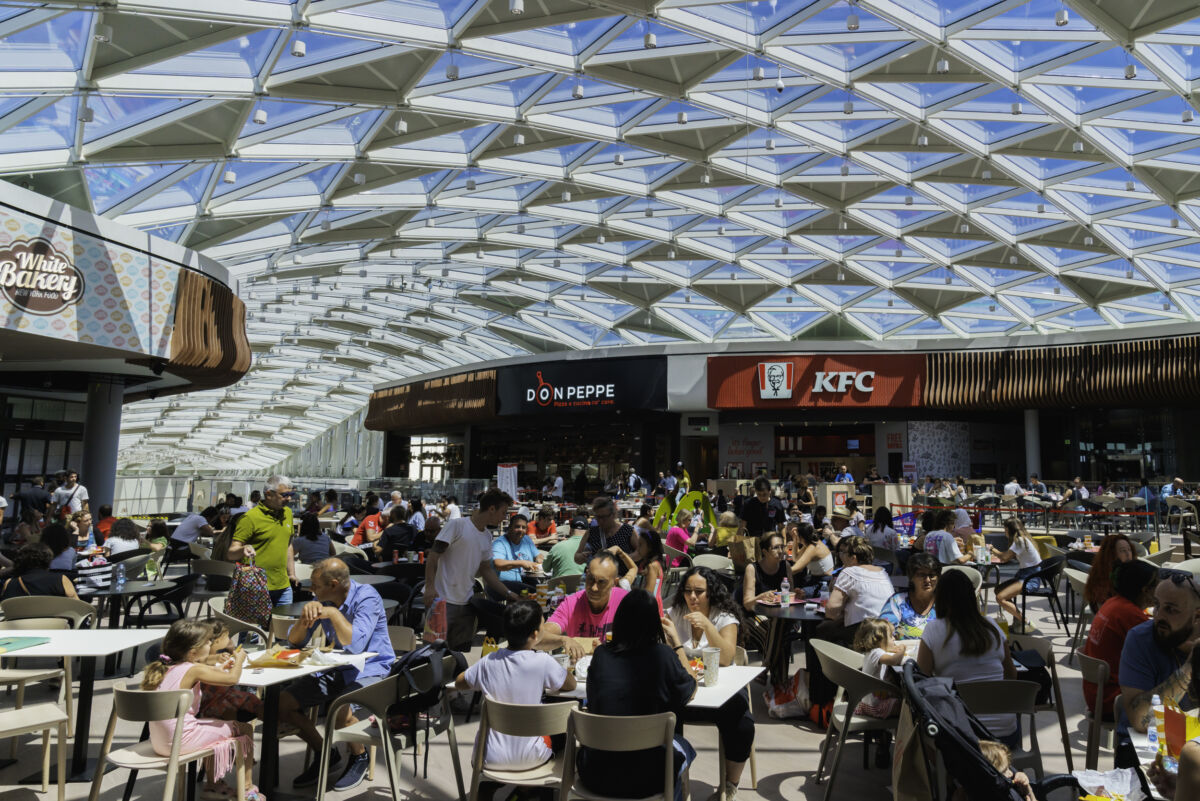 Area ristorazione affollata. Persone ai tavoli, fast food come KFC e Don Peppe.