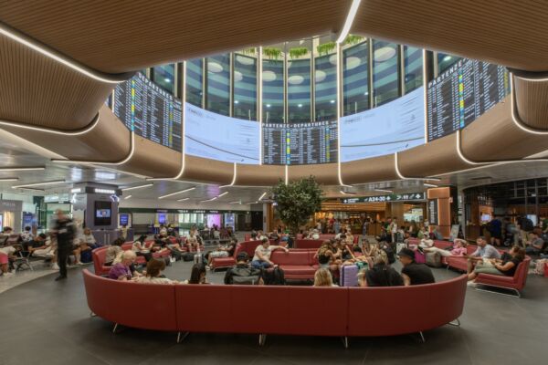 Area food court al Terminal 1 di Malpensa. Persone sedute, schermi partenze.