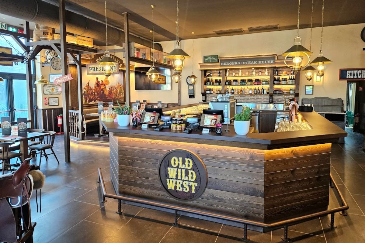 Interno ristorante Old Wild West: bancone in legno con logo, illuminazione calda e arredamento western.