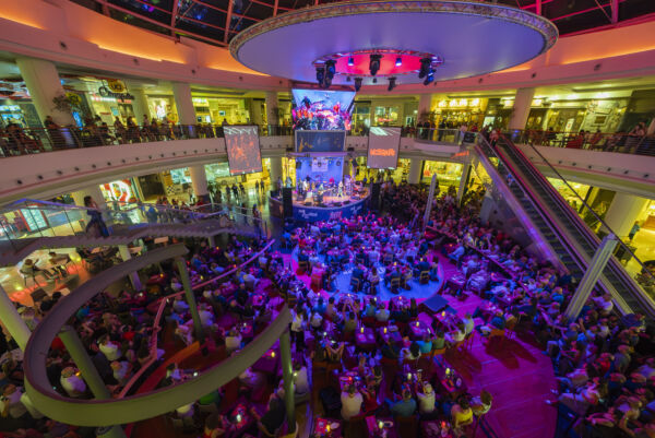 Folla al food court con musica dal vivo. Evento affollato, luci colorate.